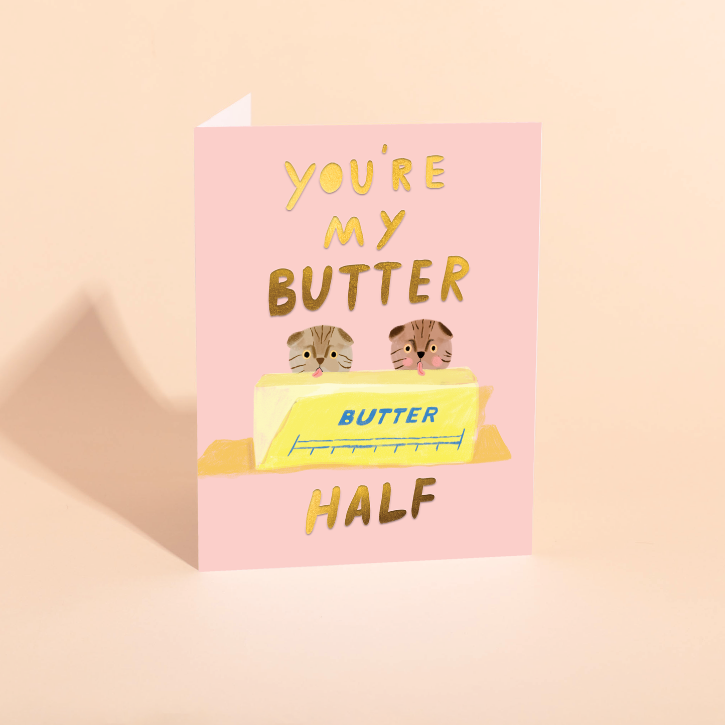 Greeting card with an illustration of two cats licking a stick of butter and text that says "you're my butter half" on a pink background