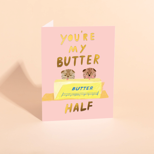 Greeting card with an illustration of two cats licking a stick of butter and text that says "you're my butter half" on a pink background
