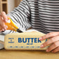 Person putting scissors into a pouch labeled 'Butter' on a wooden surface.