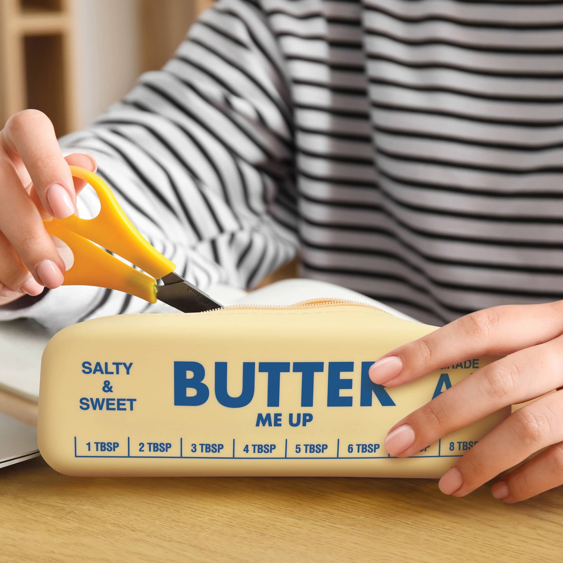 Person putting scissors into a pouch labeled 'Butter' on a wooden surface.