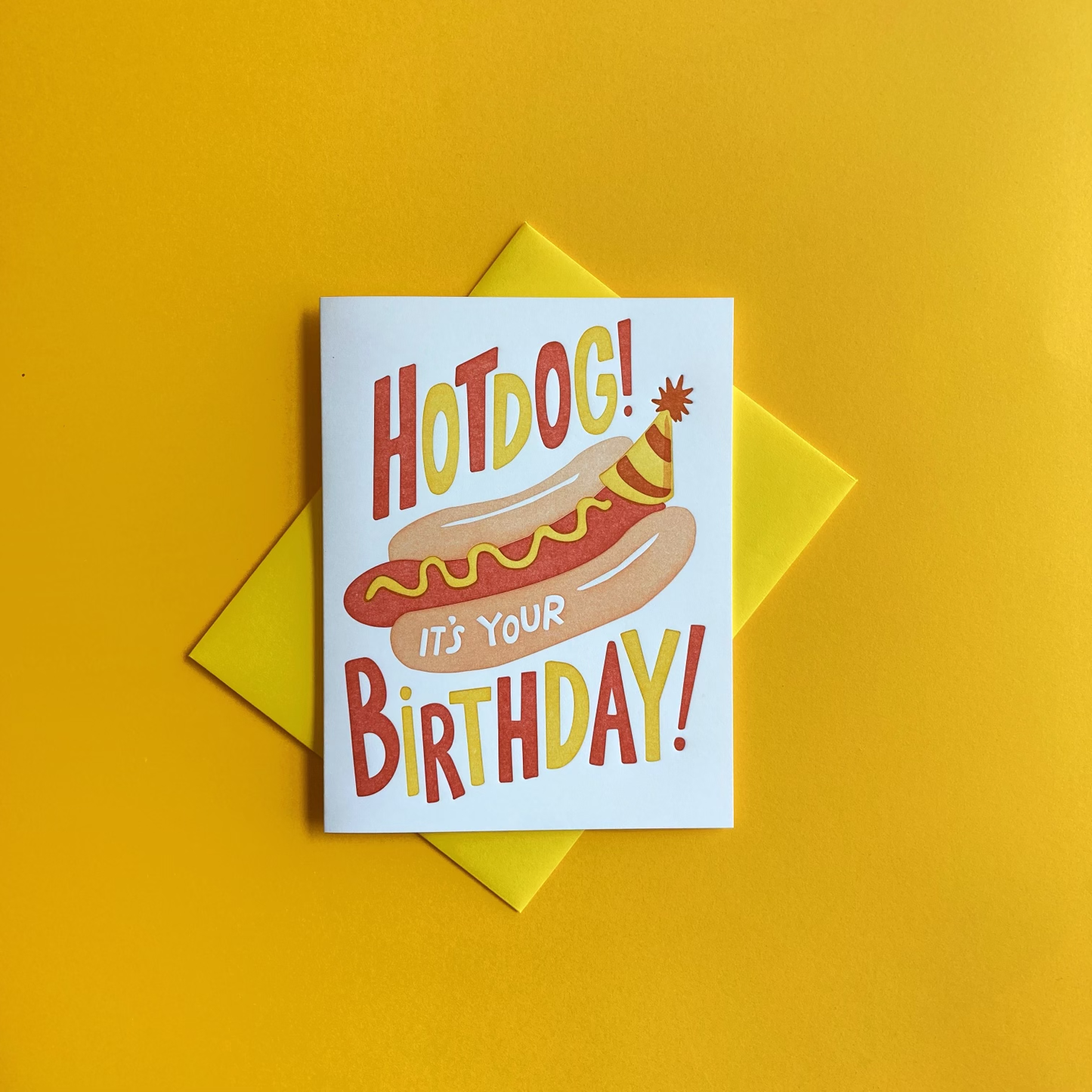 Greeting card with a yellow envelope -- text reads "Hotdog! it's your birthday!" with an image of a hot dog in a bun with mustard on it, wearing a birthday party hat