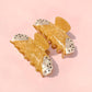 Pair of yellow cannoli-shaped hair clips on a pink background