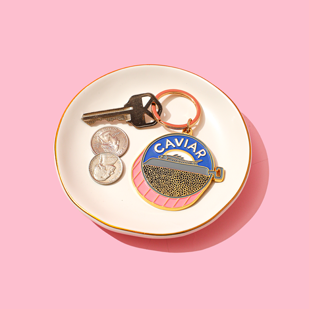Keychain with 'Caviar' branding on a white dish with coins and keys against a pink background