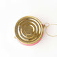 Gold and pink circular bottom of a caviar tin ornament on a white background