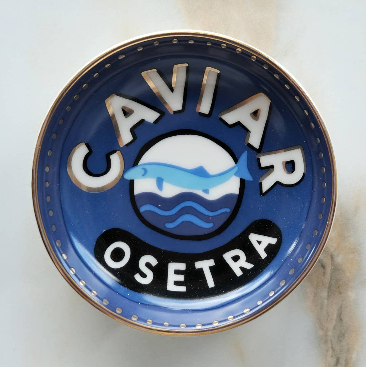 Caviar Osetra logo on a blue and gold trinket dish with a marble background