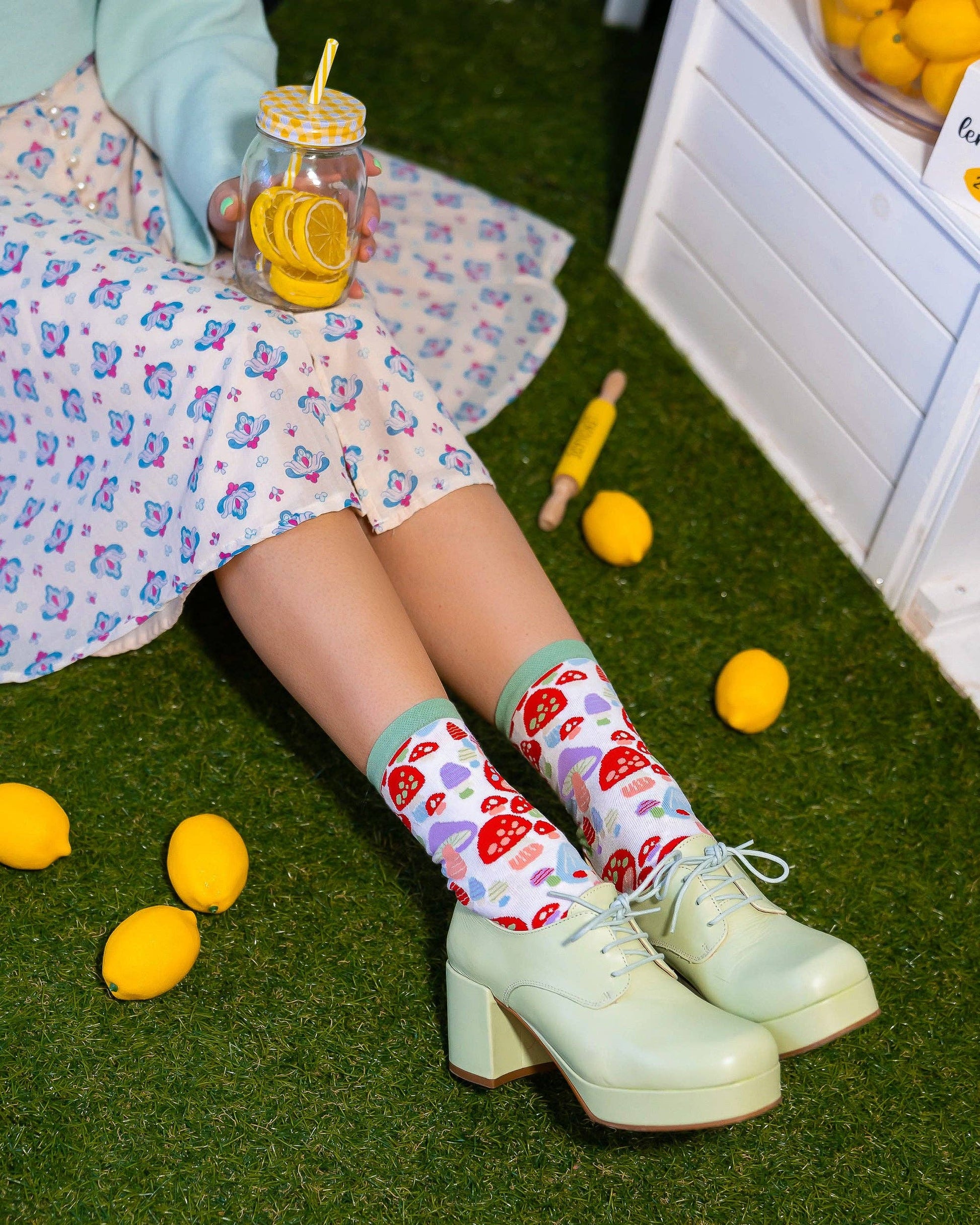 Mushroom socks with forest green toe and heel. Model is sitting on astroturf with rings on her fingers and lemonade