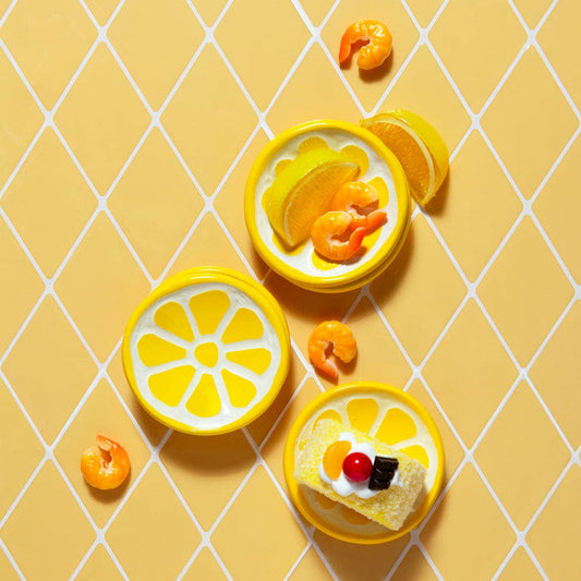Three small lemon slice shaped ceramic dishes with decorative elements on a yellow grid background