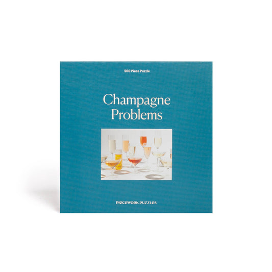 Front of Champagne Problems puzzle box. Image of puzzle with information in silver on deep blue background.