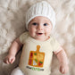 Baby wearing a onesie with a charcuterie design on a fluffy white surface