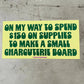 Yellow bumper stickerwith green text that reads "on my way to spend $150 on supplies to make a small charcuterie board" on a concrete surface