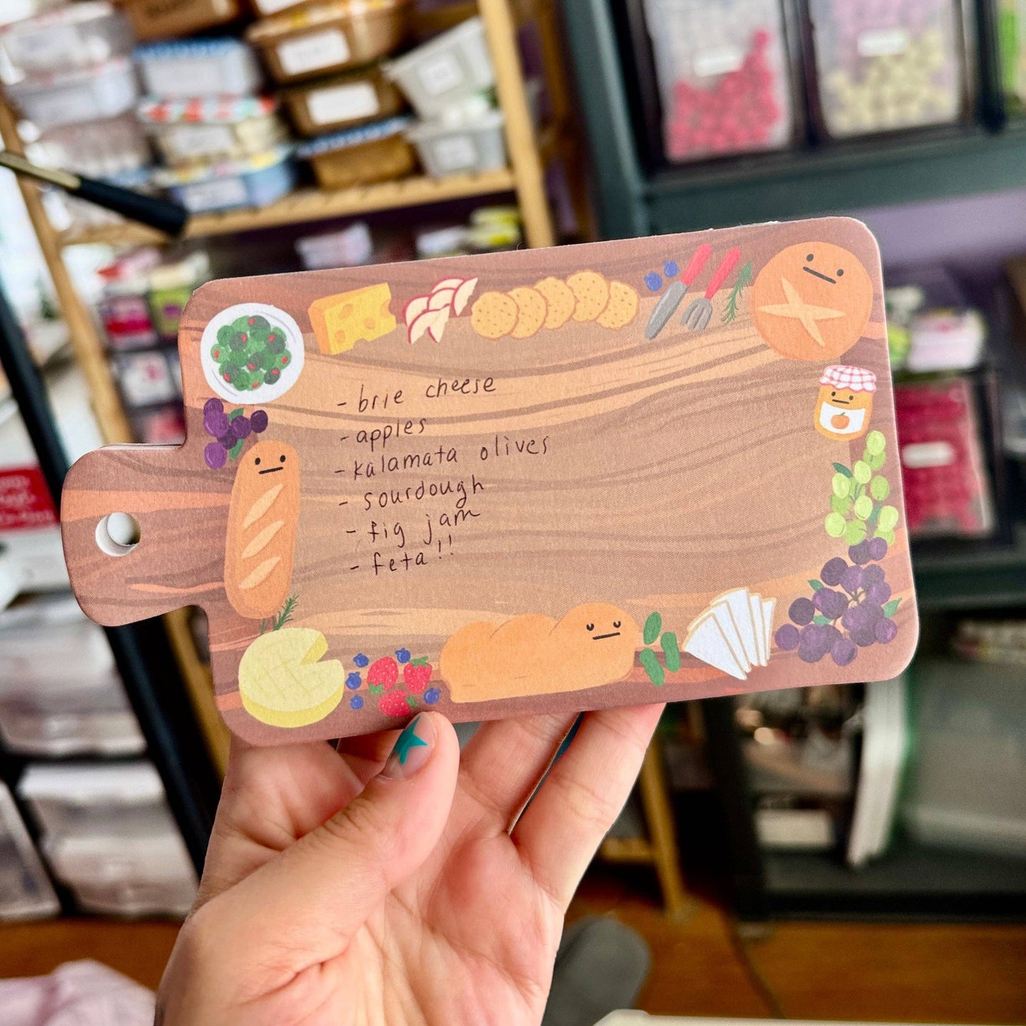 notepad shaped like a charcuterie board held in front of a store shelf