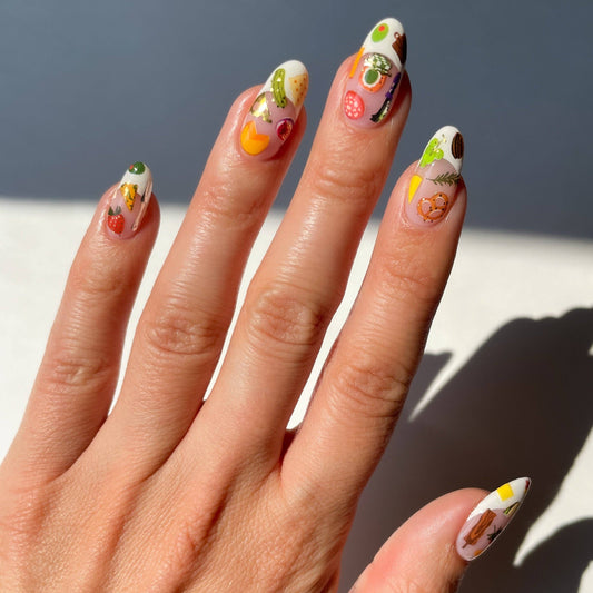 Hand with intricately designed nails featuring various charcuterie-themed designs against a neutral background