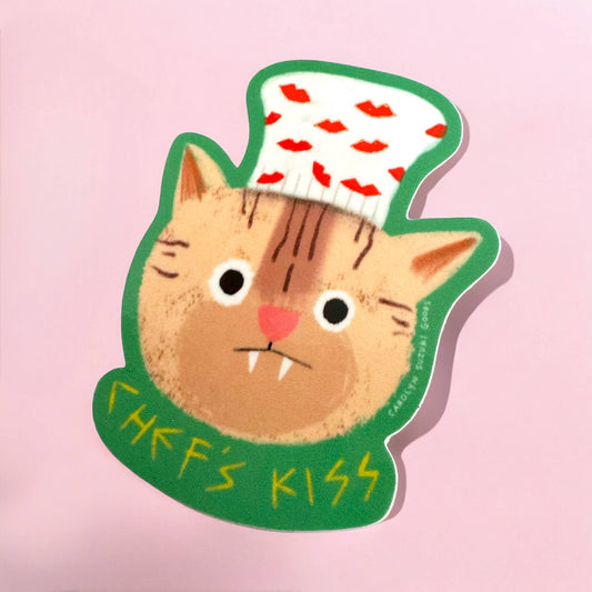 sticker of a cat with fangs wearing a white chef's hat with red lips on it and text at the bottom that reads "Chef's Kiss" 