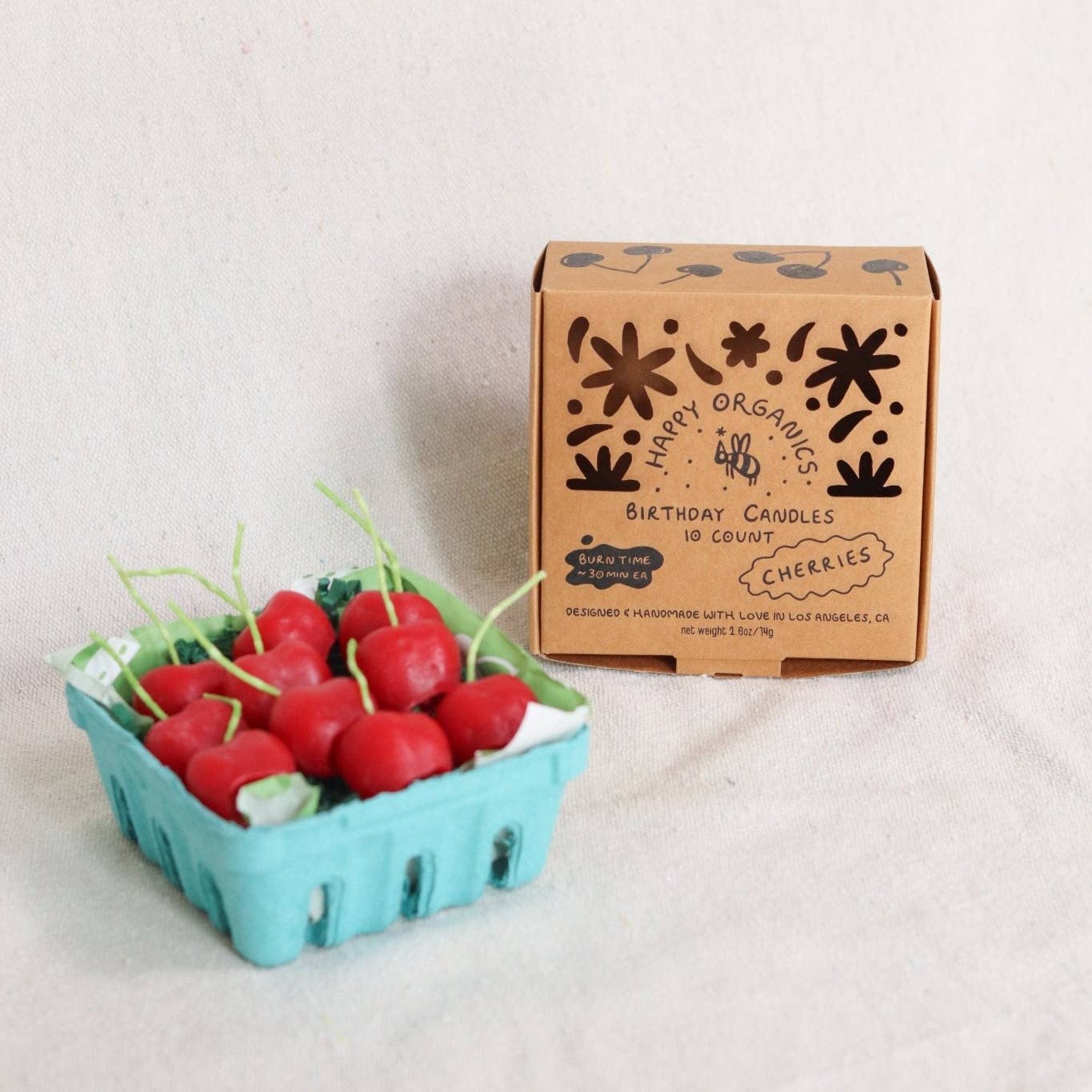 Box of Happy Organics birthday candles shaped like cherries next to a container of small red fruits.