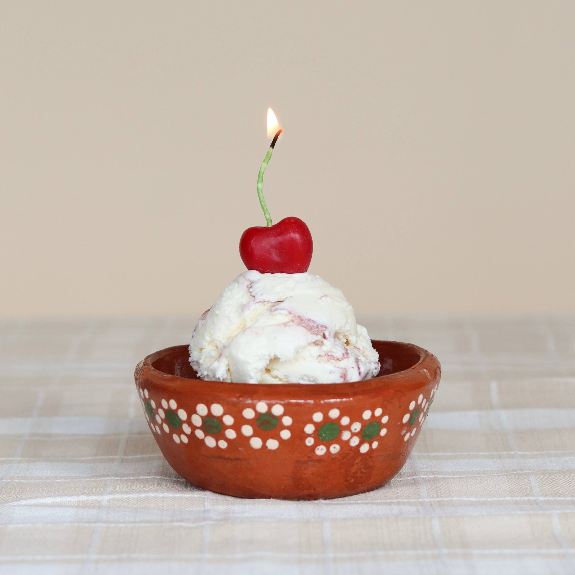 Ice cream bowl with cherry shaped candle on a checkered tablecloth