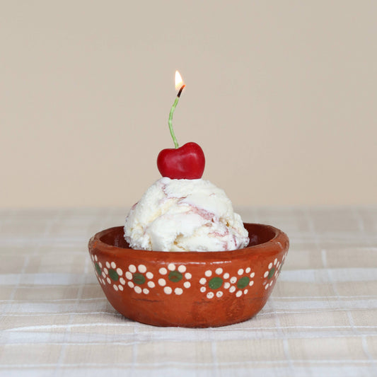 Ice cream bowl with cherry shaped candle on a checkered tablecloth