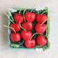 Box of red cherry candles with green stems on a light background