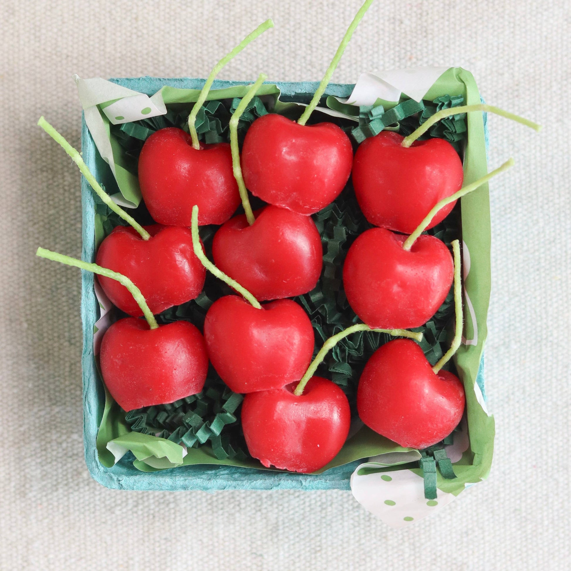 Box of red cherry candles with green stems on a light background