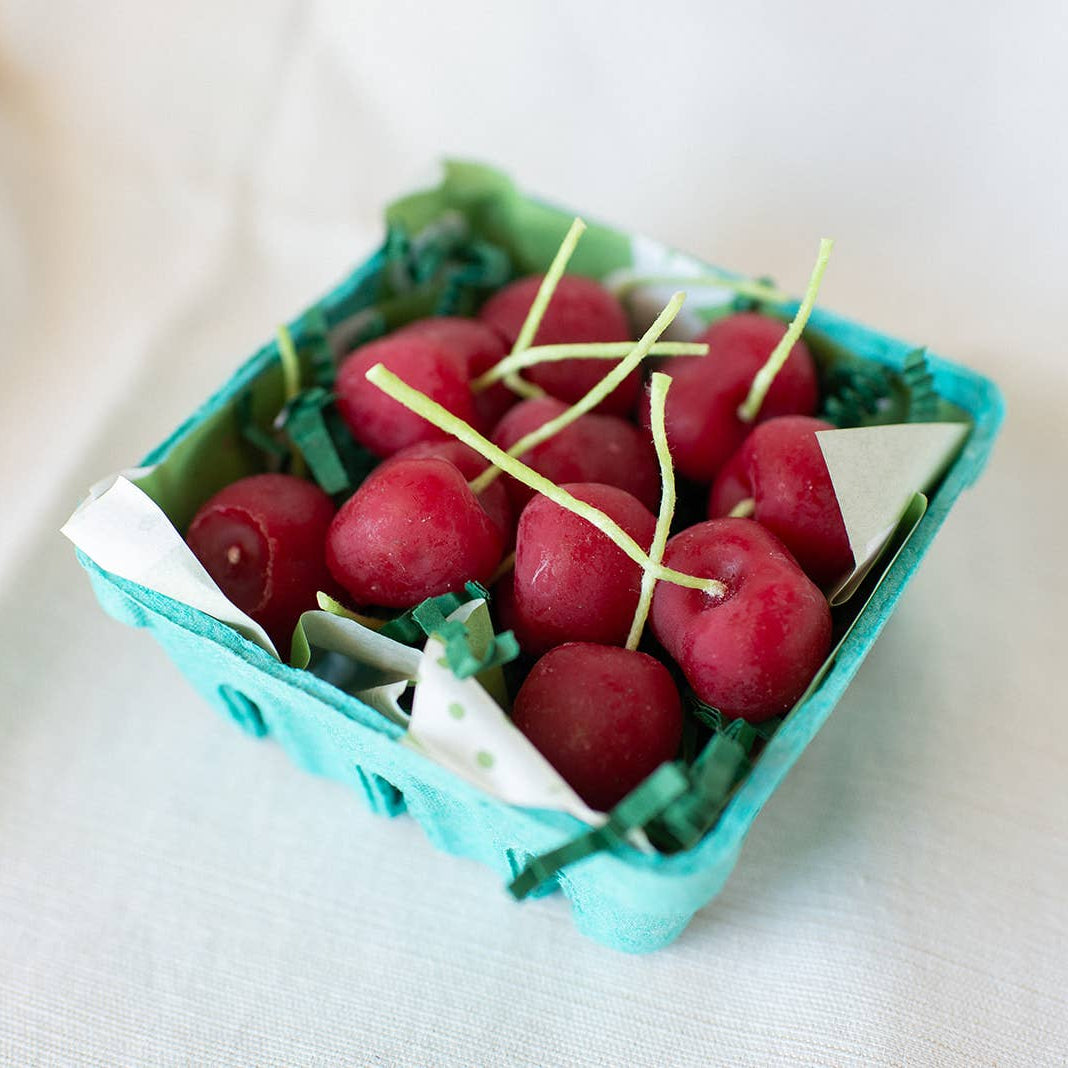 Small turquoise container with cherry shaped candles on a light background