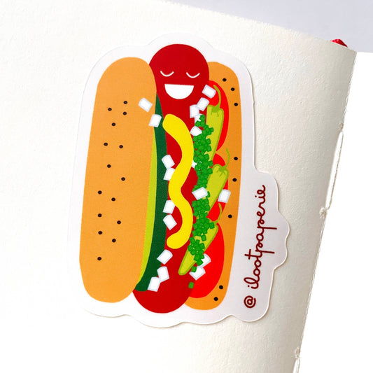 Sticker of a hot dog with mustard, ketchup, onions, pickle spears, peppers and relish on a white background