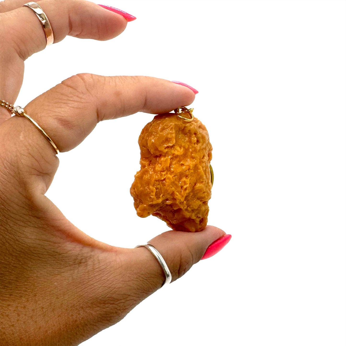 Hand holding a small chicken nugget shaped keychain against a white background