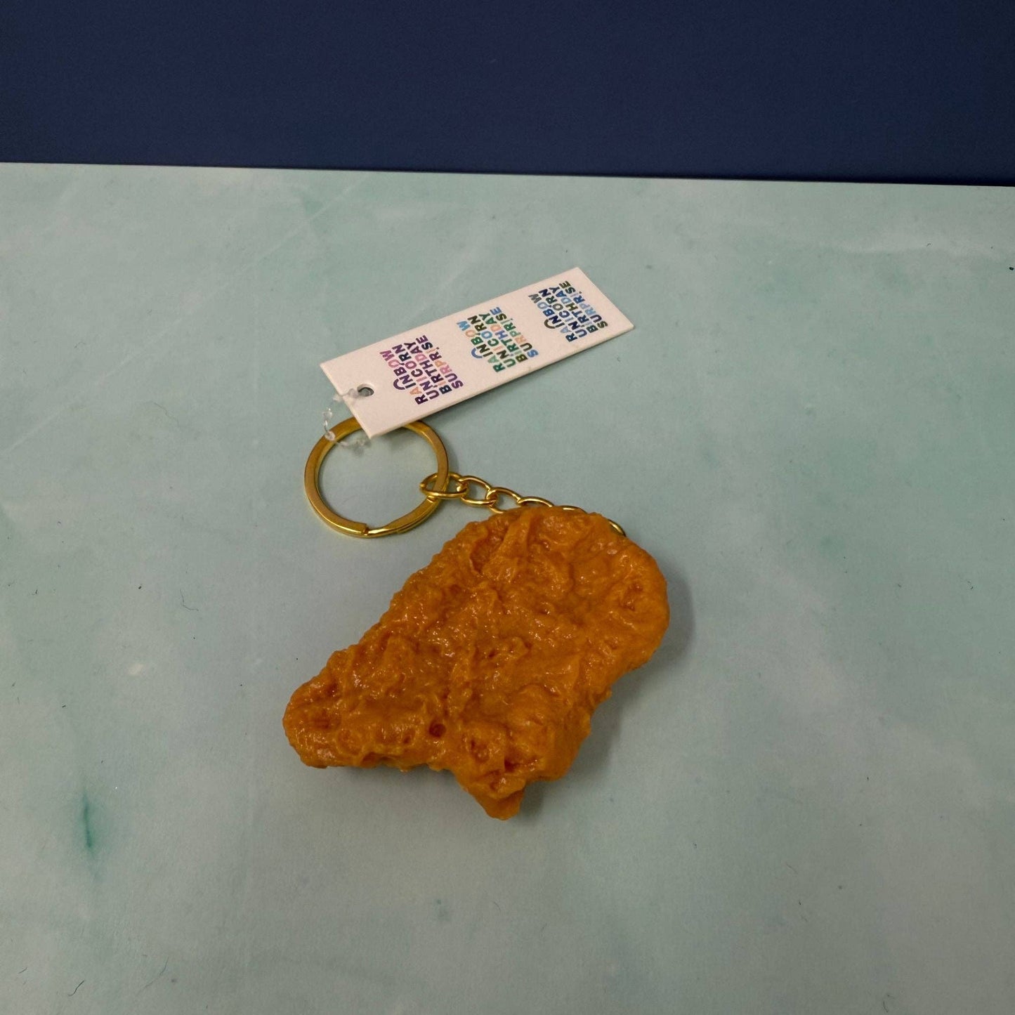 chicken nugget shaped keychain with a gold ring on a light green surface with a blue background