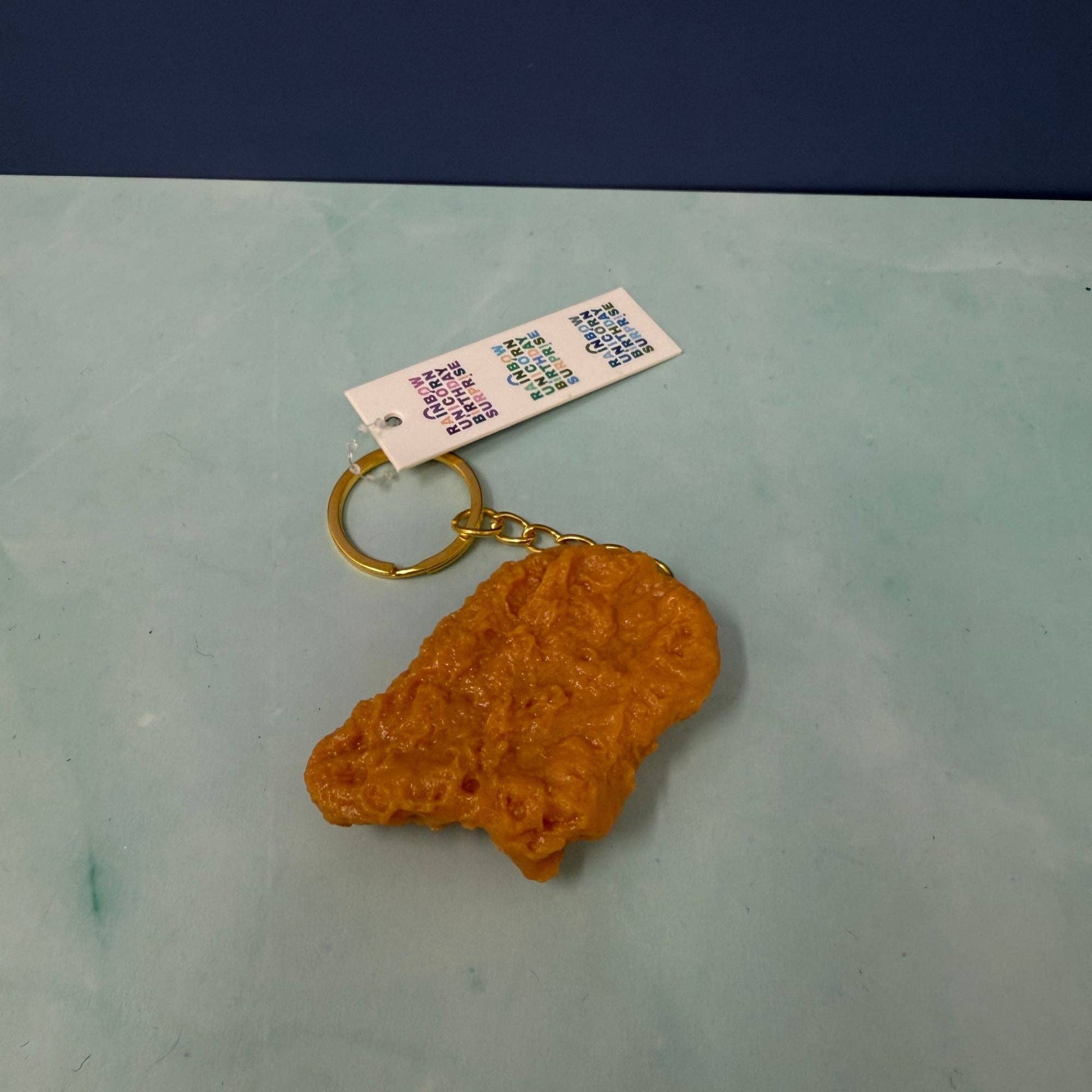 chicken nugget shaped keychain with a gold ring on a light green surface with a blue background