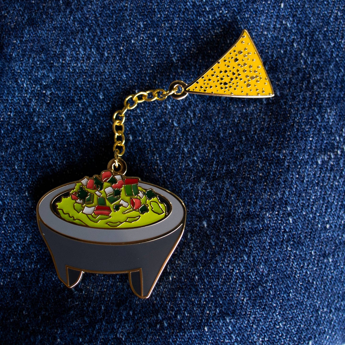 enamel pin of guacamole in a molcajete and a single tortilla chip, attached by chain