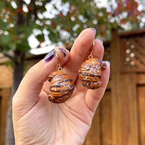 Hand holding a pair of earrings that look like chocolate croissants 