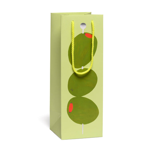 Green gift bag with 3 cocktail olives on a pick with a yellow handle on a white background