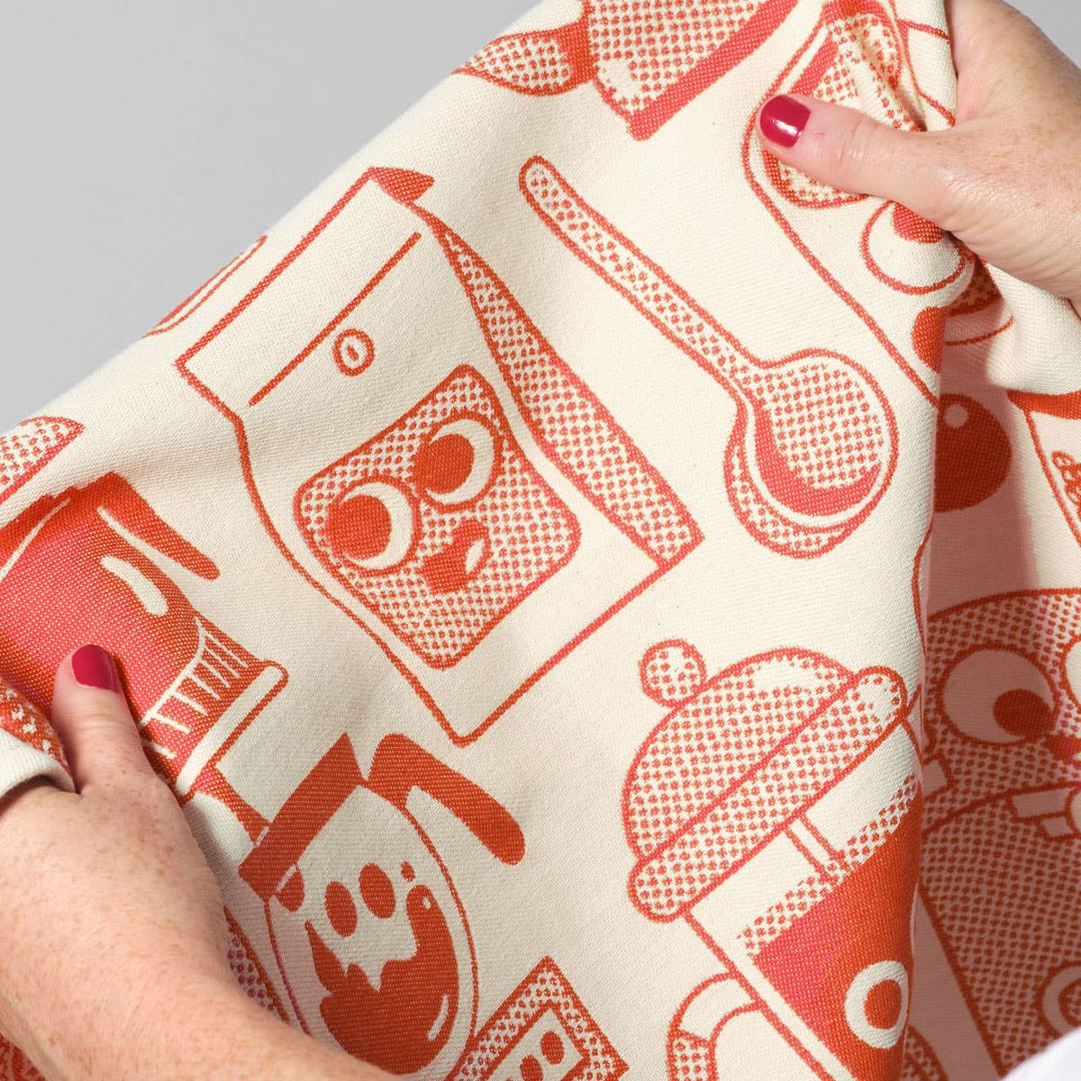 Person holding a kitchen towel with red coffee-themed patterns on a white background