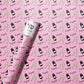 roll of wrapping paper that has a pink background with a continuous pattern of a champagne bottle, two flutes clinking and the text "congrats" all over 