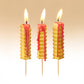 Three french fry-shaped candles with red wax drips on a beige background