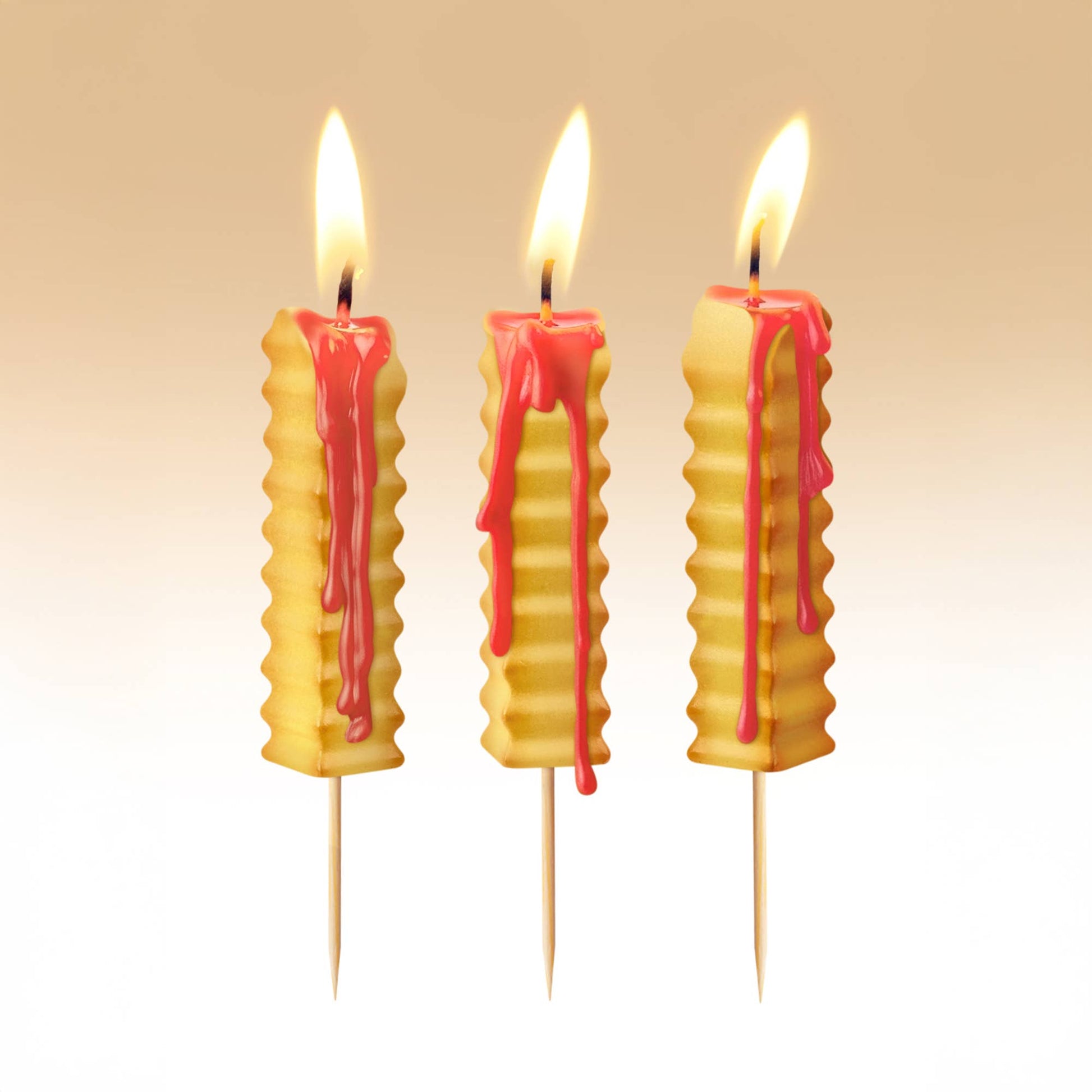 Three french fry-shaped candles with red wax drips on a beige background