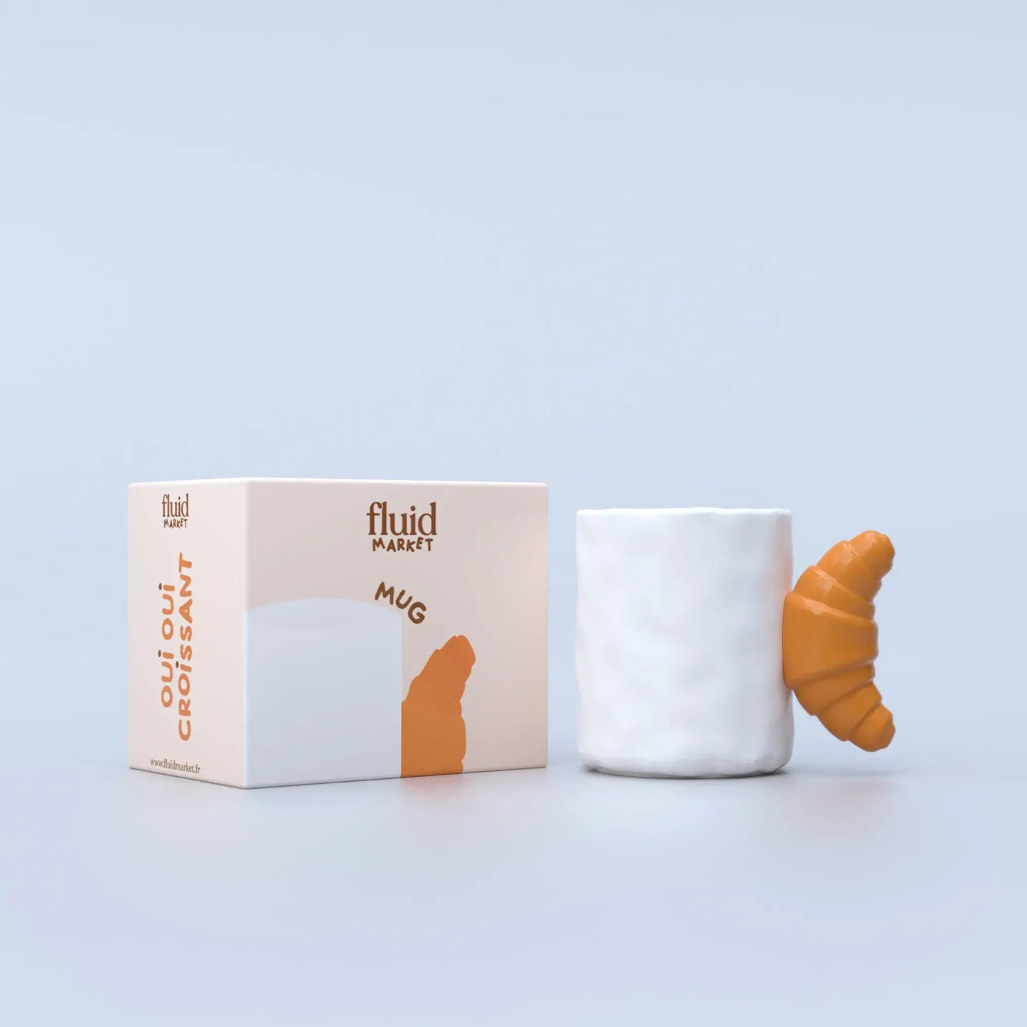 white, ceramic mug with a brown handle shaped like a croissant, photographed next to it's box packaging 