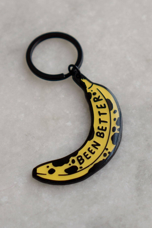  Keychain in soft enamel with matte black metal and glossy epoxy coating.  Design is a browned banana with text on it that reads "been better"