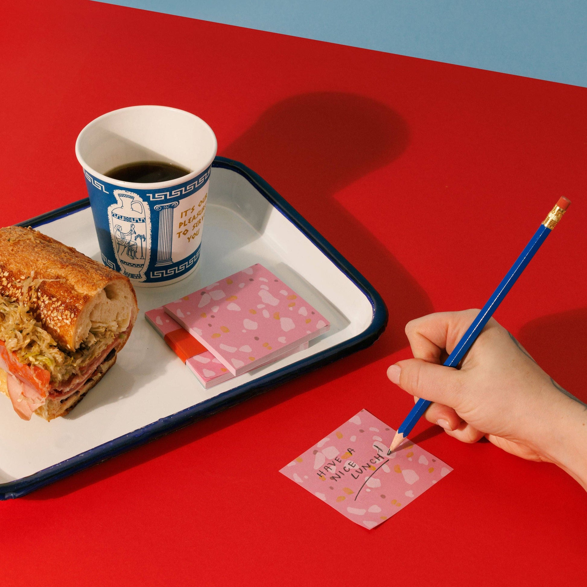 deli slice sticky notes being written on. Pictured here on a red table while someone eats a sub sandwich and has coffee 