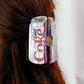 Diet Coke can-shaped hair clip on a person's hair against a white background