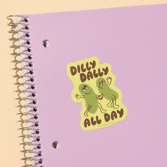 sticker with two pickles holding hands and text that reads "Dilly dally all day" on purple notebook 