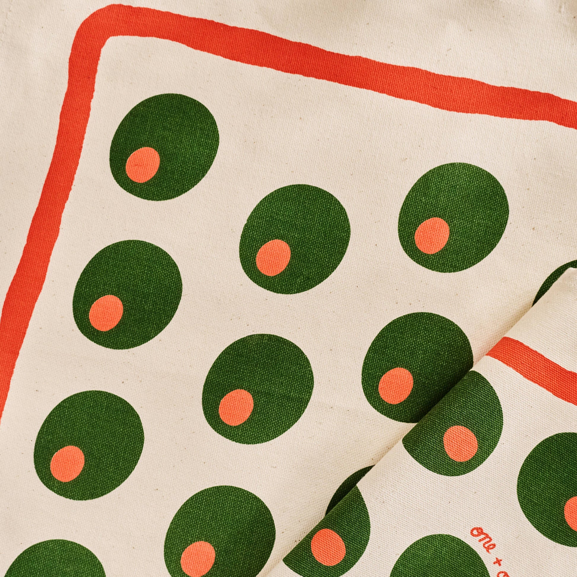 Fabric with pimento stuffed green olives pattern on a beige background and red line border along edge