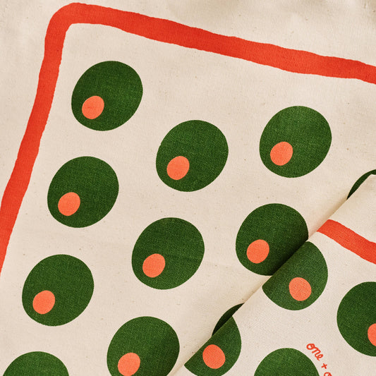 Fabric with pimento stuffed green olives pattern on a beige background and red line border along edge