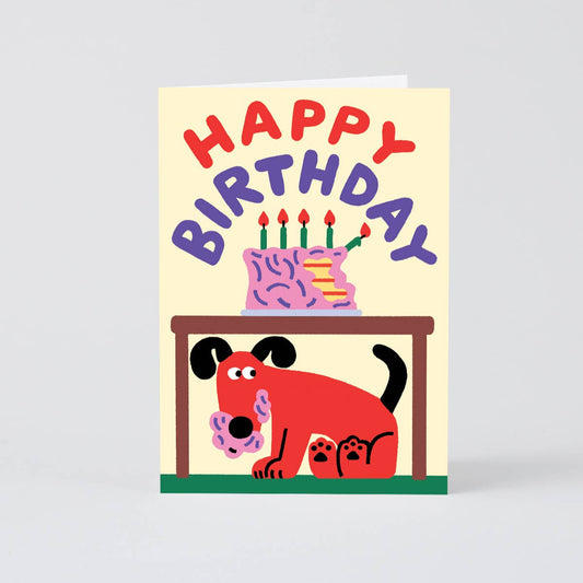 birthday greeting card with illustration of a cake on top of a table with a mischievous dog underneath with frosting all over it's mouth