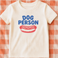 White t-shirt with 'DOG PERSON' and a hot dog graphic on a red and white checkered background