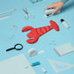 Red lobster-shaped pouch on a blue background with stationery items.