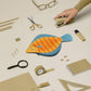 Plaice fish case sitting among beige stationery-ware for size and color reference.