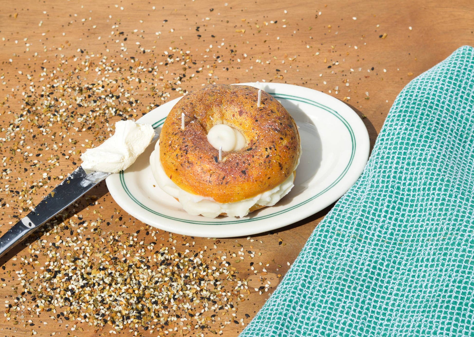 Everything bagel candle shown on a plate with a knife full of cream cheese.