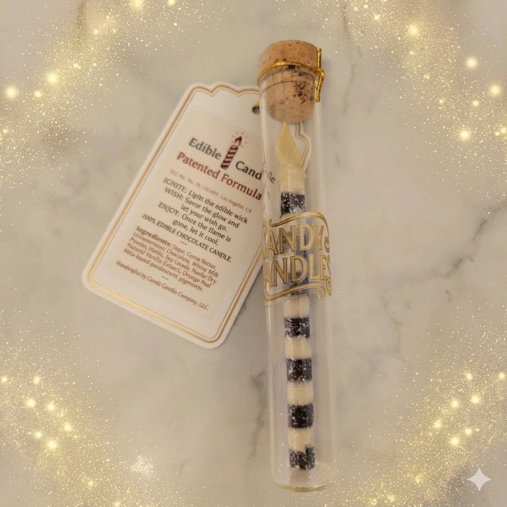A glass tube candle with a cork stopper and gold seal, containing a black-and-white striped wax candle, shown with a printed product tag on a light marble surface with a sparkling overlay.