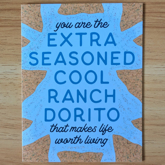Card with blue text featuring a humorous message, "you are the extra seasoned cool ranch dorito that makes life worth living" on a wooden surface.