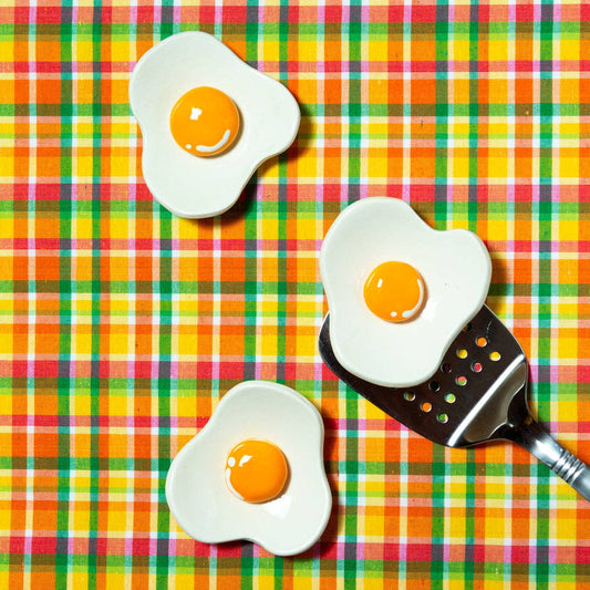 Three ceramic egg dishes on a colorful checkered background