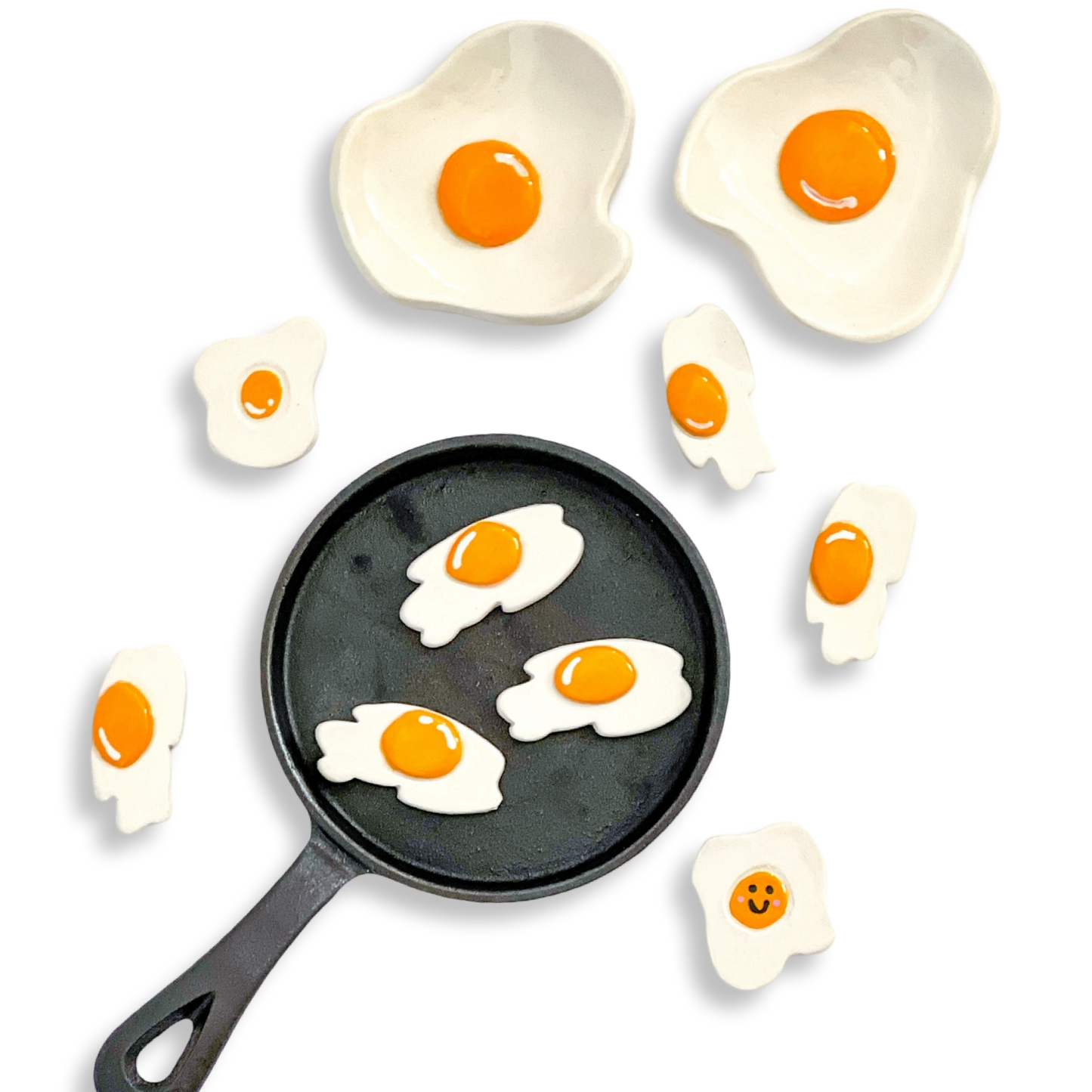 Black frying pan with ceramic egg dishes around it on a white background